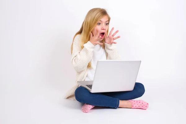白人少女坐在笔记本电脑前 背对着白皙的莲花 脸上带着震惊的表情 手拉手靠近脸庞 尖叫着 侧视着令人惊奇的东西 — 图库照片