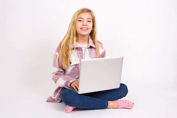 美しいですCaucasianティーン女の子座っていますノートパソコンで蓮の位置に白の背景で幸せと面白いです顔笑顔とショー舌 — ストック写真