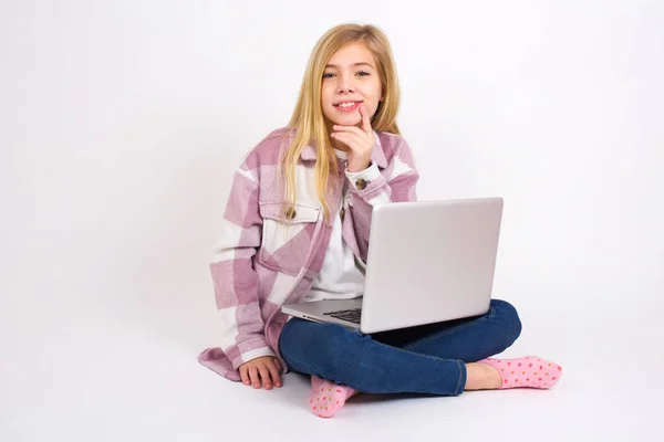 注意してください成功した美しい白人のティーンの女の子は白い背景にハスの位置にノートパソコンで座って白い歯を喜んで輝く頭を傾けるカメラを見つめ顎を触れます 歯科医療の概念 — ストック写真