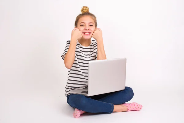 幸せな美しいですCaucasianティーン女の子座っていますノートパソコンでハスの位置にホワイトバックグランドキープ拳上の頬笑顔広くと持っています肯定的な式あります良い気分 — ストック写真
