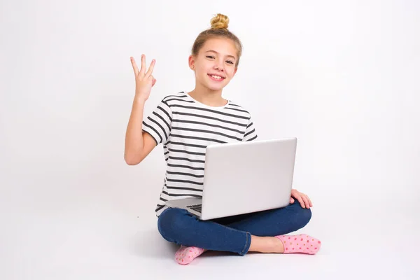 美しいですCaucasianティーン女の子で座ってノートパソコンでハスの位置に白い背景笑顔と友好的に見えます 前方に手で数3番目または3番目を示します カウントダウン — ストック写真