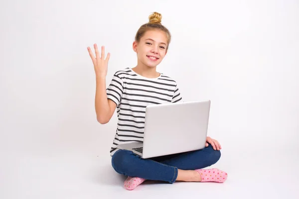 美しいですCaucasianティーン女の子で座ってノートパソコンでハスの位置に白い背景笑顔と友好的に見えます 番号4または4を示します前方に手で カウントダウン — ストック写真