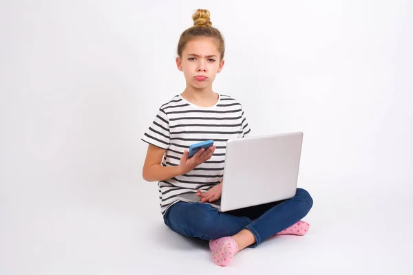 動揺不満美しいですCaucasianティーン女の子で座っているラップトップでハスの位置に白の背景にモバイルソフトウェアアプリケーションを使用し インターネット上の情報をサーフ 保持しています現代のモバイル手 — ストック写真
