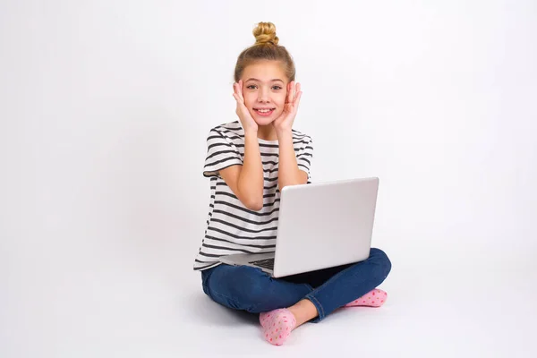 幸せな美しいですCaucasianティーン女の子で座ってノートパソコンでハスの位置に白い背景の両方の頬に優しく触れます 優しい笑顔を持っています 白い歯を示しています 積極的にカメラでまっすぐ — ストック写真