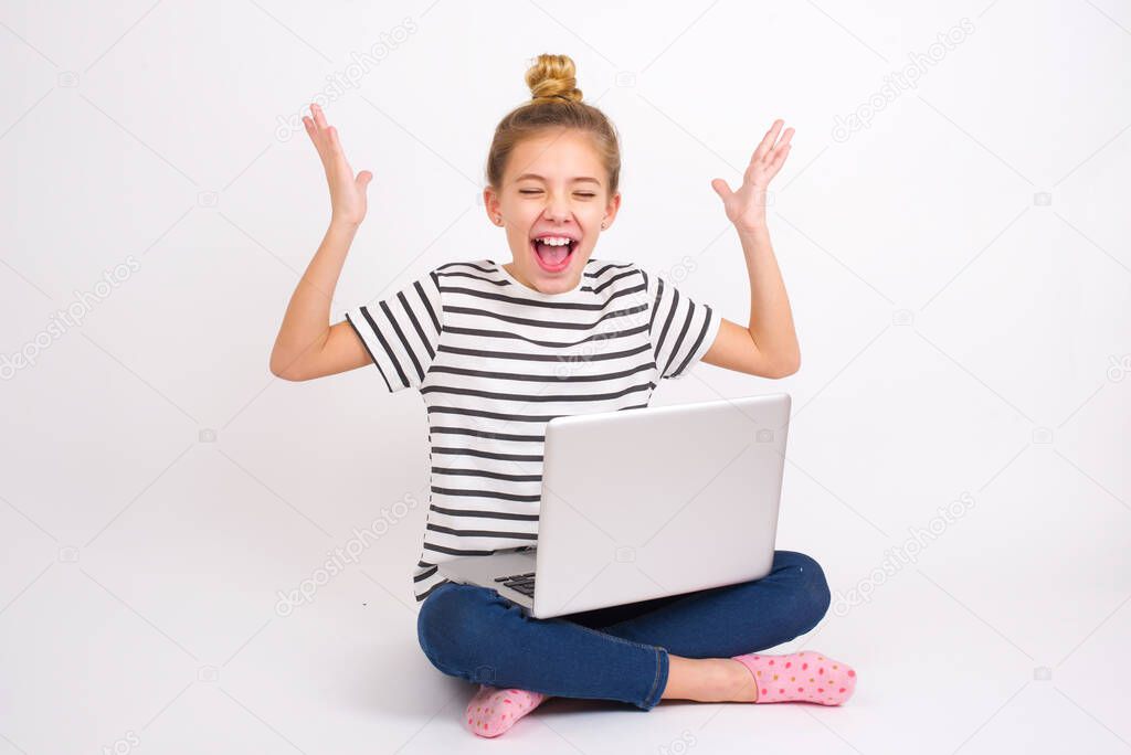 Beautiful caucasian teen girl sitting with laptop in lotus position on white background goes crazy as head goes around feels stressed because of horrible situation