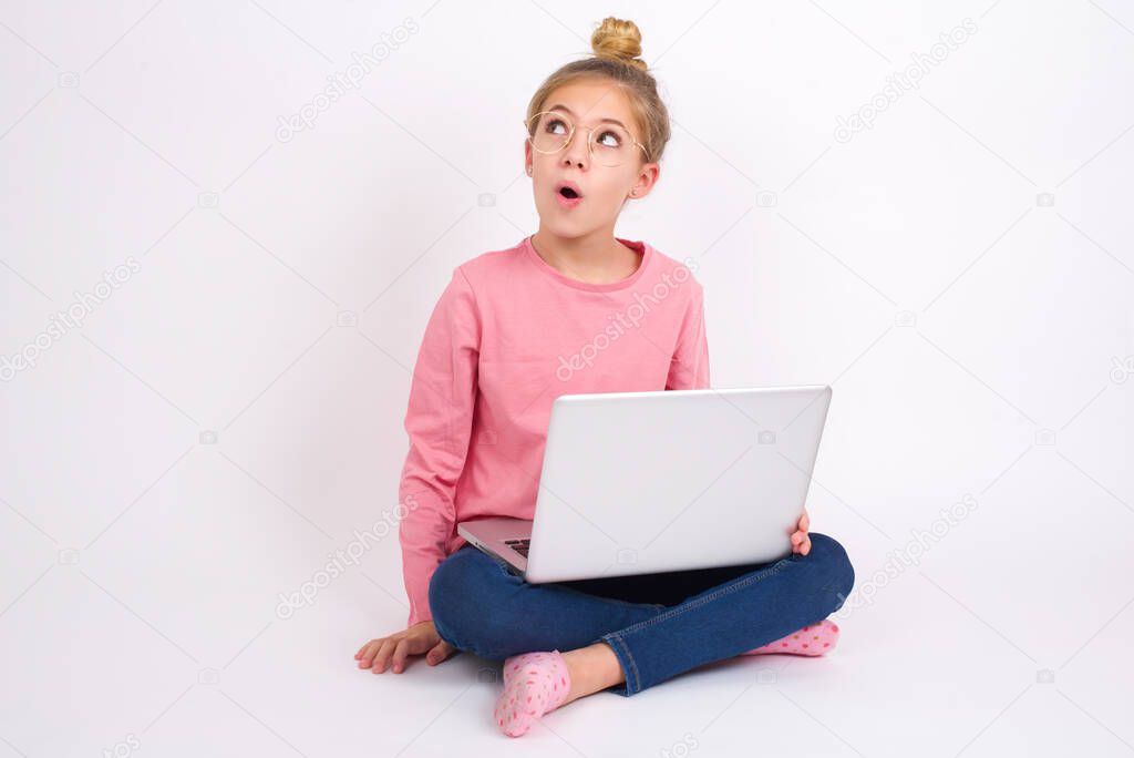 Shocked Beautiful caucasian teen girl sitting with laptop in lotus position on white background look empty space with open mouth screaming: Oh My God! I can't believe this.
