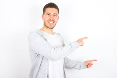 Beyaz arka plan noktalarının üzerine gündelik kıyafetler giyen genç beyaz bir adam ağzı açık şaşkın bir ifadeyle şaşırtıcı bir şey gösteriyor. Reklam kavramı.