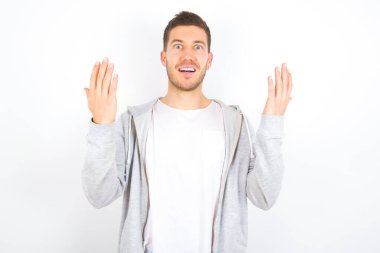 Neşeli, şanslı, beyaz arka planda günlük kıyafetler giyen beyaz bir adam. Tezahürat yapıyor, başarıyı kutluyor, yumruklarını sıkarak evet diye bağırıyor.