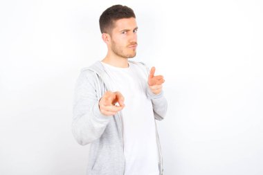 Hey sen, bang. Neşeli ve karizmatik yakışıklı beyaz arka planda günlük giysiler giyen beyaz adam göz kırpıyor ve kameraya mutlu ve küstah bir şekilde parmak tabancalarıyla işaret ediyor..