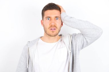 Kafası karışmış, beyaz arka planda günlük kıyafetler giyen beyaz saçlı, kaşlarını çatan, panikleyen ve hafızasını kaybeden beyaz bir adamın portresi. Endişeli ve endişeli. Hiçbir şey hatırlayamıyor..