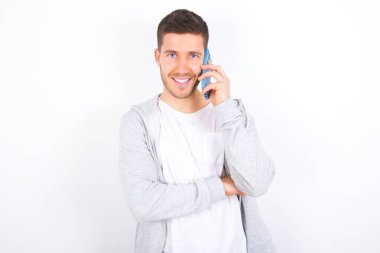 Beyaz arka planda günlük giysiler içinde cep telefonuyla konuşan gülümseyen beyaz bir adamın portresi. İş, güven ve iletişim kavramı.