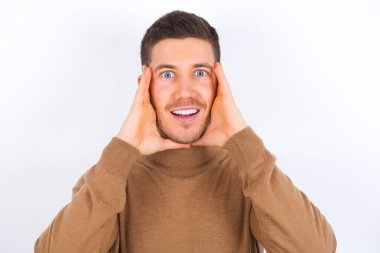 Beyaz arka plan üzerine balıkçı yaka giyen genç beyaz bir adam neşeli ve neşeli görünüyor.