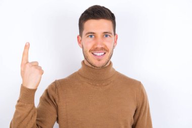 Beyaz arka plan üzerine balıkçı yaka giyen genç beyaz bir adam gülümsüyor ve arkadaş canlısı görünüyor, bir ya da ilk eli önde, geriye doğru sayıyor.