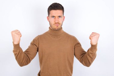 Sinirli, genç, beyaz bir adam öfkeyle yanaklarına vurur ve yumruklarını kaldırır. Öfke ve agresif duyguları ifade eder. Öfkeli model