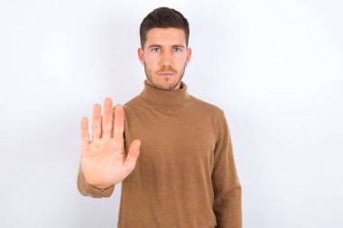 Genç beyaz adam dur işareti gösteriyor. Yasak işareti. Avuç içini kameraya sert bir ifadeyle yaklaştırıyor.