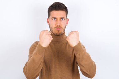 Displeased annoyed  man  clenches fists, gestures pissed, ready to revenge, looks with aggression at camera stands full of hate, being pressured