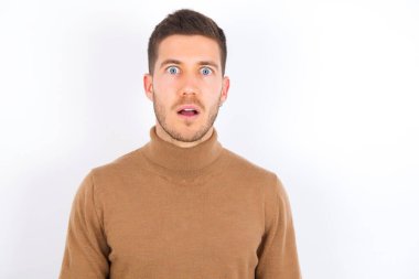 Şok olmuş, beyaz arka plan üzerine balıkçı yaka giyen genç, beyaz gözlü, ağzı açık bakan, şaşırmış bir ifadeye sahip. Omg kavramı