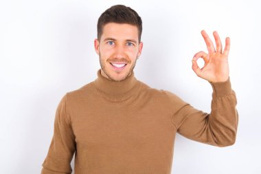 Beyaz arka plan üzerine balıkçı yaka giyen genç beyaz adam el ele tutuşuyor. Tamam, dişlek onaylı haber tavsiyesi.