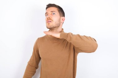 Beyaz arka plan üzerine balıkçı yaka giyen, boğazını bıçak niyetine kesen, saldırganlığı şiddetle tehdit eden genç beyaz bir adam..