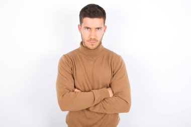Beyaz arka plan üzerine balıkçı yaka giyen neşeli, kendinden emin, genç beyaz bir adamın fotoğrafı.