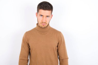 Beyaz arka plan üzerine balıkçı yaka giyen genç beyaz bir adam depresif ve üzüntülü, sinirli ve korkmuş bir şekilde ağlıyor. Üzücü ifade.