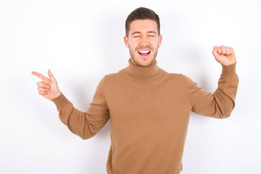 Beyaz arka plan üzerine balıkçı yaka giyen neşeli beyaz bir adam fotokopi alanı reklamını göstererek şansı kutluyor.