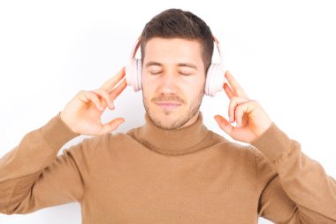 Beyaz arka plan üzerine balıkçı yaka giyen memnun genç beyaz adam, hoş melodiyi dinlemekten zevk alır. Ses kulaklığı takar, gözleri kapatır. Müzikle boş zaman geçirmek