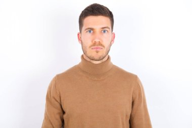 Beyaz arka plan üzerine balıkçı yaka giyen hoşnutsuz genç beyaz bir adam mutsuz görünüyor. Bazı sorunları var. Olumsuz duygular ve duygular konsepti