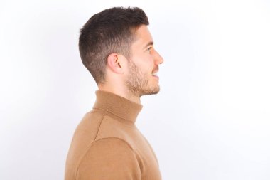 Beyaz arka plan üzerine balıkçı yaka kazak giyen hoş beyaz bir adamın profil portresi dişlek gülüşlü boş boşluğa bakıyor