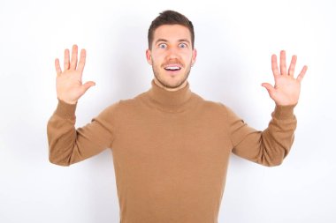 Beyaz arka plan üzerine balıkçı yaka giyen genç, keyifli beyaz adam harika bir sonuç elde ettikten sonra ağzını ve kollarını kaldırır.