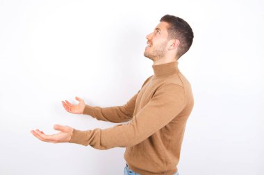 Beyaz arka plan üzerine balıkçı yaka giyen, kolları açık, boş boşluğa bakan, beyaz yakalı, komik, genç beyaz bir adam..