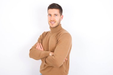 Beyaz arka plan üzerine balıkçı yaka giyen beyaz bir adamın portresi. Kollarını kavuşturup gülümsüyor.