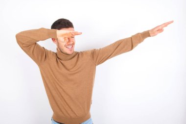 Beyaz arka planda balıkçı yaka kazak giyen, disko hareketlerini gösteren komik beyaz bir adamın fotoğrafı.