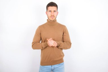 Beyaz arka plan üzerine balıkçı yaka giyen neşeli, kendinden emin, genç beyaz bir adamın fotoğrafı.