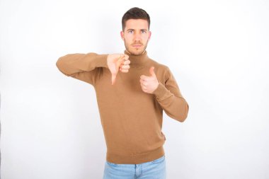  Beyaz arka plan üzerine balıkçı yaka giyen beyaz tenli beyaz bir adam baş parmağını aşağı işareti olarak gösteriyor.