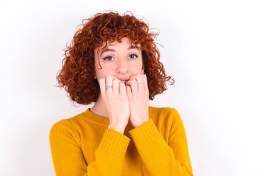 Endişe - beyaz arka planda sarı süveter giyen genç bir kızıl kız. Ağzını ellerle kapatıyor. Bir şeyden ya da birinin tırnak yemesinden korkuyor..