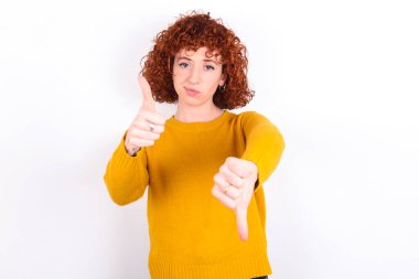 Beyaz arka planda sarı süveter giyen genç, kızıl saçlı kız kötü bir işaret verdiğinden emin olamıyor. Memnun değil ve etkilenmemiş..