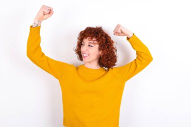 Evet, ben kazandım. Beyaz arka planda sarı süveter giyen, mutlu ve heyecanlı genç bir kızın portresi zafer ve zafer içinde yumruk kaldırıyor ve mutluluktan sırıtarak başarı elde ediyor..