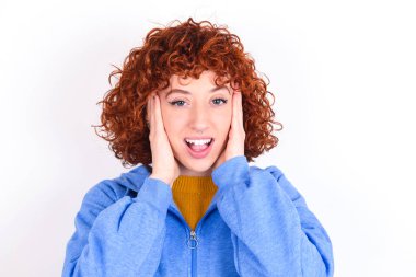 Beyaz arka planda mavi ceketli genç kızıl kız neşeli ve mutlu görünüyor.