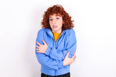 Beyaz arka planda mavi ceketli genç bir kız. Kış soğuğu yüzünden titriyor ve donuyor. Yüzünde üzgün ve şok ifadesi var..