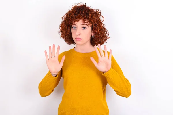 穿着黄色毛衣 披着白色背景的红头发少女 别再用手掌唱歌了 脸上带有消极而严肃的手势的警告表情 — 图库照片