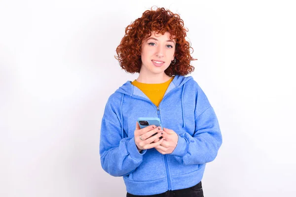 Молодая Рыжая Девушка Синей Куртке Белом Фоне Использование Мобильного Телефона — стоковое фото
