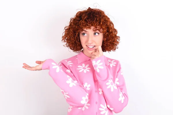 正面的红头发少女穿着粉色花T恤 头戴白色背景广告 用手指触摸牙齿 — 图库照片