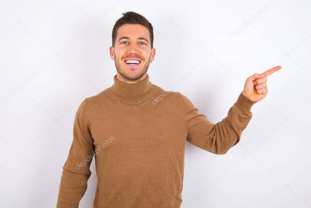 young  caucasian man  laughs happily points away on blank space demonstrates shopping discount offer, excited by good news or unexpected sale.