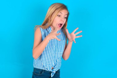 Yüzünde şok ifadesi olan beyaz bir kız çocuğu, yüzünün yanında el ele tutuşuyor, çığlık atıyor ve şaşırtıcı bir şeye yan gözle bakıyor..