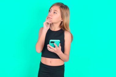 Siyah spor kıyafetler giyen, yeşil arka planda cep telefonu kullanan ve el ele tutuşan küçük bir kız çocuğu hayal etmeyi düşünüyorum. Karar almak ve sosyal medya kavramı.