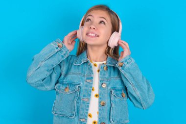 Mavi arka planda kot ceket giyen neşeli sarışın kız çocuğu şarkı söylüyor. Mikrofon sanki en sevilen müzik listesini kulaklıkla dinliyormuş gibi el altında tutuyor.