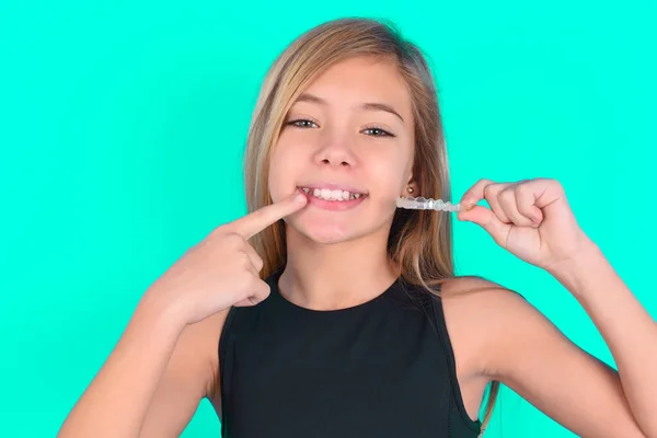 girl   holding an invisible aligner and pointing to her perfect straight teeth. Dental healthcare and confidence concept.