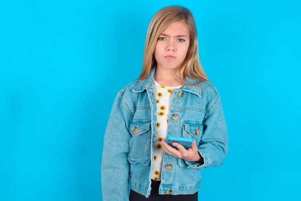 デニム ジャケットを身に着けている不満の金髪の慎重な少女はモバイル ソフトウェア アプリケーションを使用し インターネットのシェフの情報は現代移動式手を握ります — ストック写真