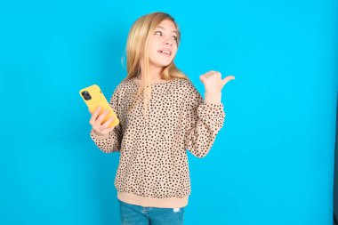 Kafkasyalı kız akıllı telefonuyla mesaj atıyor ve gülümseyen yüzüyle başparmağıyla işaret ediyor.